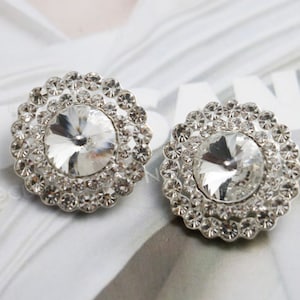May include: A pair of silver tone earrings with a large clear rhinestone centre surrounded by smaller rhinestones.