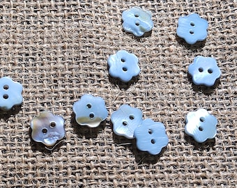 May include: A collection of nine small, flower-shaped buttons crafted from iridescent mother-of-pearl. Each button features a smooth, glossy surface with a subtle sheen and two central holes for attachment, displaying natural variations in color.