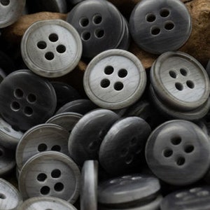 May include: A pile of gray plastic buttons with four holes each. The buttons have a slightly textured surface.