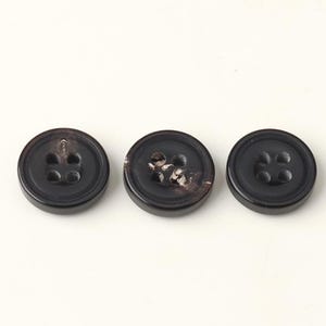 May include: Three dark brown buttons with four holes each, arranged horizontally. The buttons have a slightly glossy finish and a classic, round shape. The buttons are suitable for various sewing projects.