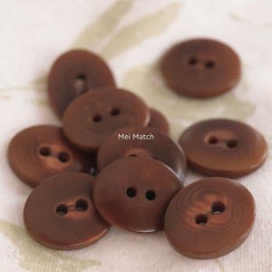 May include: A collection of round, brown buttons, each featuring two central holes for attachment. The buttons have a smooth, slightly glossy finish with subtle circular grain patterns. The text Mei Match is visible in the center.