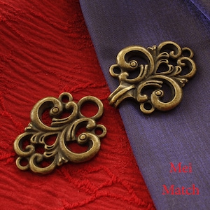 Puede incluir: Dos cierres decorativos de metal dorado antiguo con intrincados diseños de volutas. Los cierres están sobre un fondo de tela roja y morada.