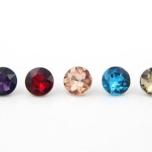May include: Five round, faceted glass rhinestones in different colours: purple, red, light pink, blue, and brown.