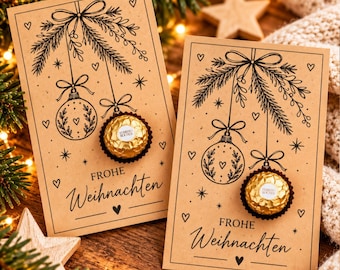 May include: Two rectangular kraft paper cards featuring black ink illustrations of hanging Christmas ornaments and pine branches. Each card has a gold foil-wrapped Ferrero Rocher chocolate attached and the text "FROHE WEIHNACHTEN" printed in black.