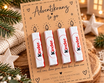 May include: A rectangular brown card featuring the text Adventskranz to go with four Kinder chocolate bars attached vertically. The card includes illustrations of four candle flames above the bars and German text below them, decorated with hearts and stars.