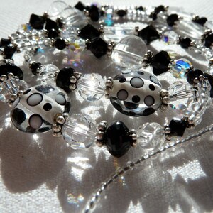 May include: A black and white beaded necklace with clear glass beads and silver accents. The necklace features large, round, polka-dotted beads.