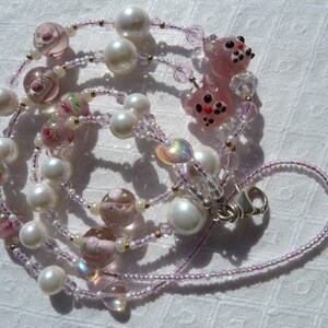 May include: A pink and white beaded necklace with floral and animal charms. The necklace has a silver clasp and is made of multiple strands of beads.
