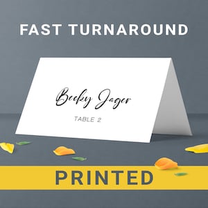 May include: White place card with black text that reads "Becky Jager" and "Table 2".