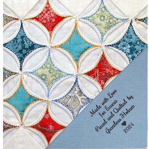 May include: A white quilt with a geometric pattern of red, blue, and gold fabric squares. The quilt is pieced and quilted by Grandma Holmes for Emma. The label is dated 2024.