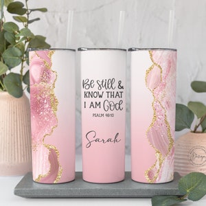 Op de afbeelding: Drie roze en gouden glitterbekers met een witte achtergrond. De middelste beker heeft de tekst "Be still & know that I am God" met "Psalm 46:10" eronder. De naam "Sarah" staat onder de tekst.