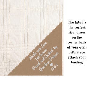 May include: A brown fabric label with white text that reads "Made with Love for Emma Pieced and Quilted by Grandma Holmes 2024". The label has a small heart symbol next to the year.