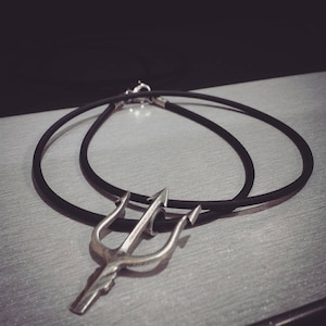 Puede incluir: Un collar con un colgante de tridente de plata en un cordón negro.