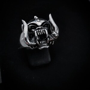 May include: A silver ring with a detailed, snarling monster head design. The monster has horns and a large mouth with sharp teeth.