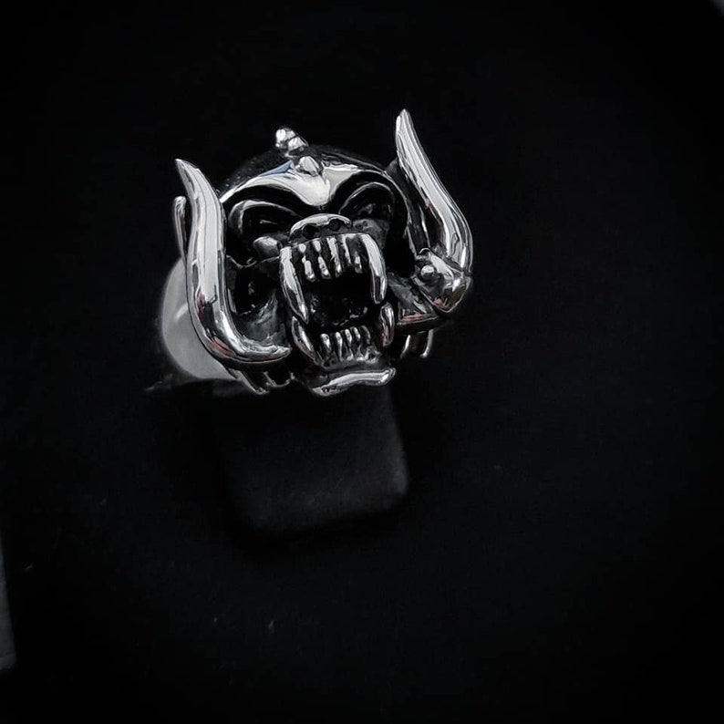 May include: A silver ring with a detailed, snarling monster head design. The monster has horns and a large mouth with sharp teeth.