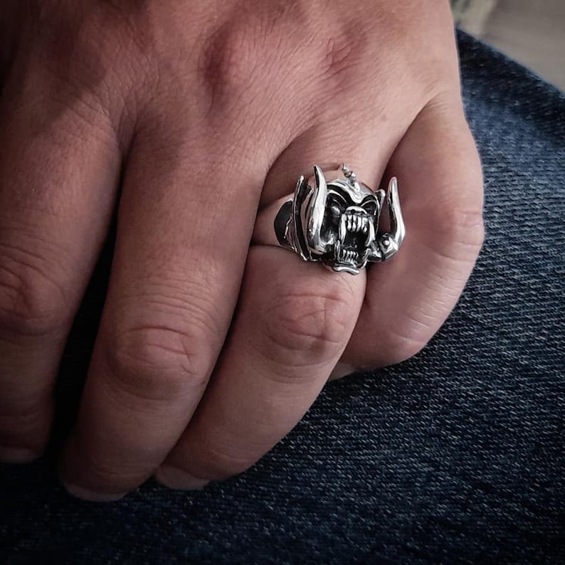 May include: A silver ring with a detailed design of a snarling monster head with horns.