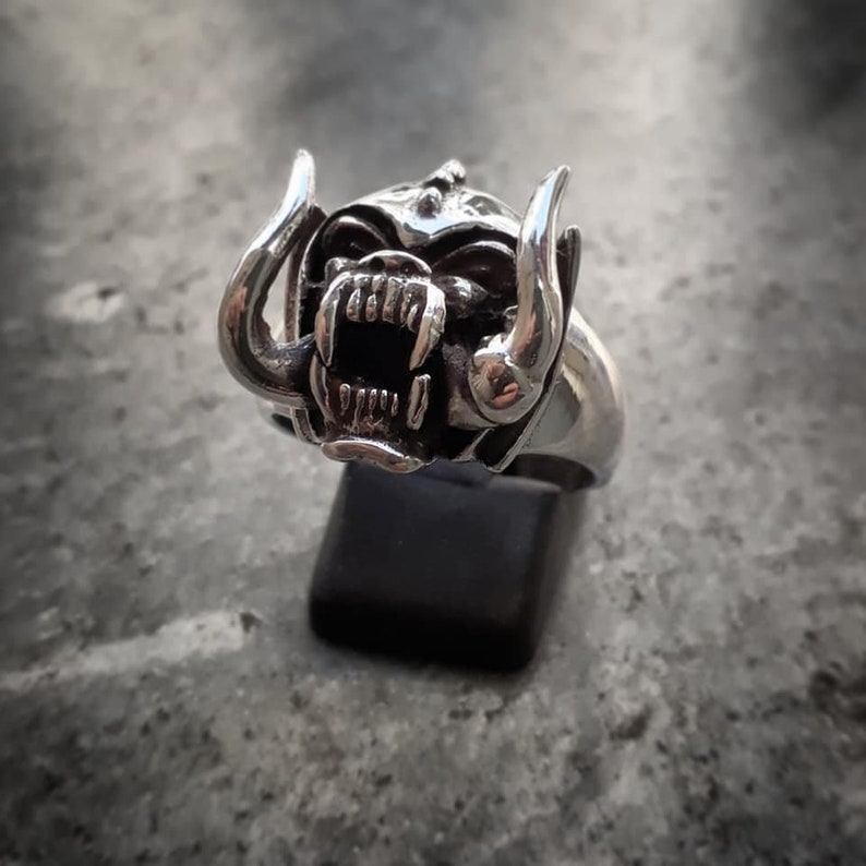 May include: A silver ring with a detailed design of a snarling monster head with horns.