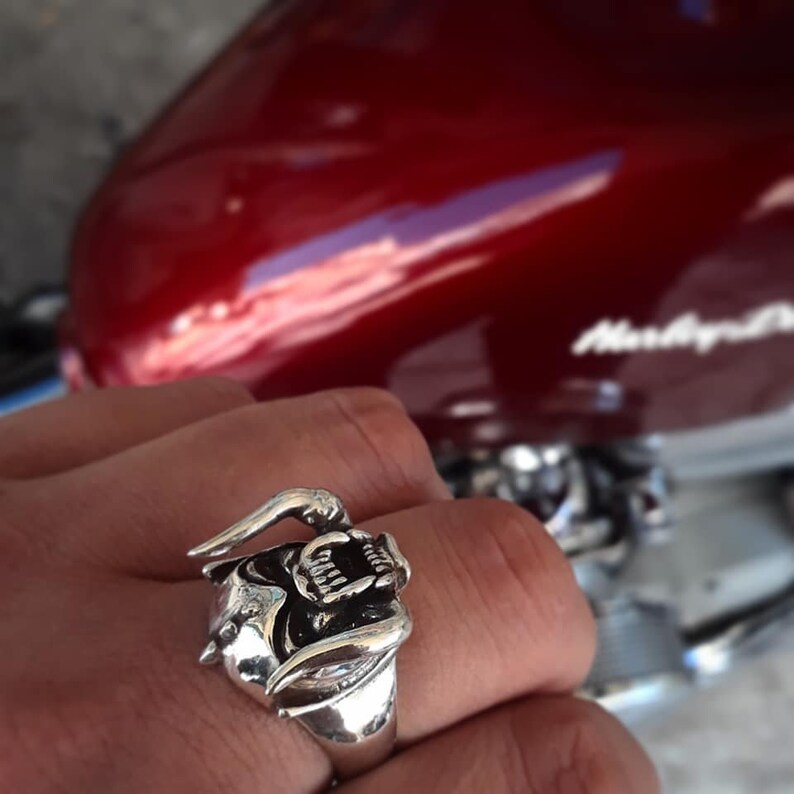 May include: A silver ring with a detailed design of a snarling animal head. The ring is worn on a person's finger.