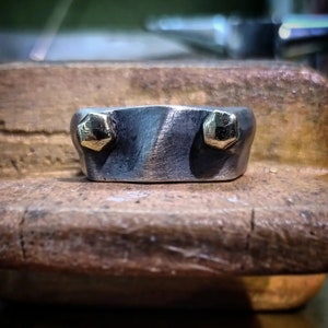May include: A silver ring with two gold accents. The ring is textured and has a unique design.