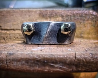 May include: A silver ring with two gold accents. The ring is textured and has a unique design.