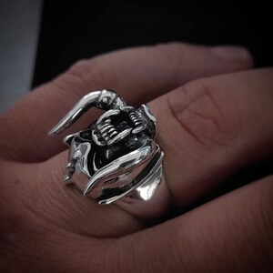 May include: A silver ring with a detailed design of a snarling beast with fangs and horns.