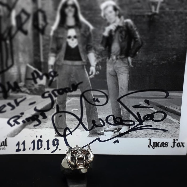 May include: A black and white photo of a band signed by the band members. The photo is signed "We are the Ring - Growler" and "Lucas Fox". The date "21.10.19" is written below the signatures. A silver ring with a detailed skull design is in the foreground.