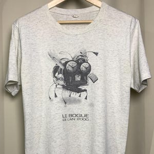 May include: A light grey heathered t-shirt featuring a black and white graphic of a mechanical creature composed of computer parts and clocks. Below the graphic, the text reads LE BOGUE DE L'AN 2000. The shirt has short sleeves and a crew neckline.