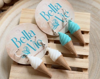 May include: A pair of ice cream cone earrings with silver hooks. The earrings are on a wooden surface with a card that says "Bella Vie" and "bellaviejewelry.com".