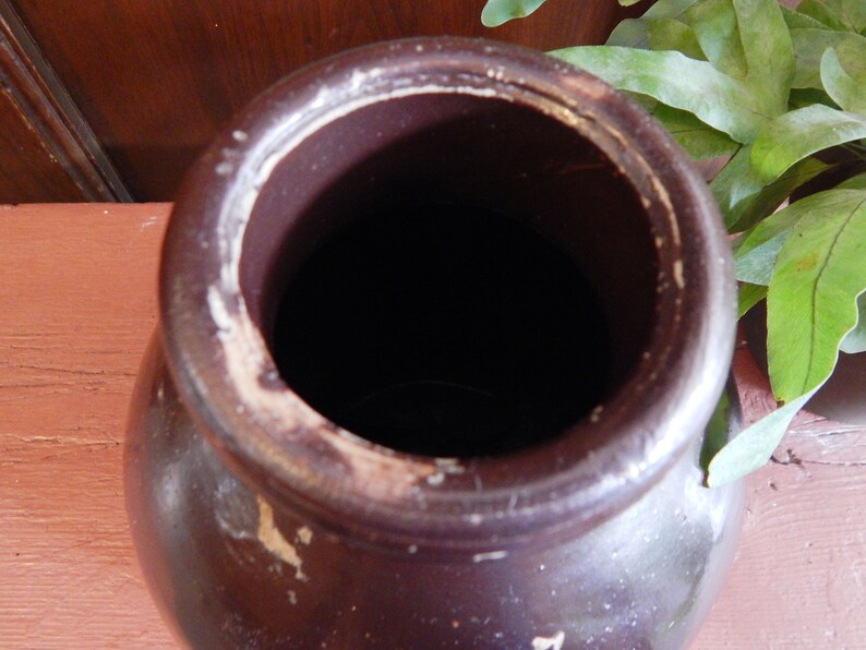 K&ouml;nnte beinhalten: Eine braune Keramik-Vase mit einer breiten &Ouml;ffnung und einem wei&szlig;en Rand. Die Vase ist leer und hat ein rustikales Aussehen.