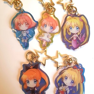 May include: Five colorful anime character keychains with gold star-shaped charms. Each keychain features a different character with a unique design and color scheme.