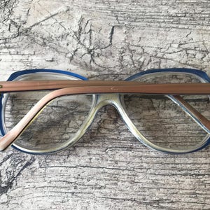May include: Vintage spectacles with a blue and clear frame and a copper-coloured bridge. The glasses have a retro design, with a rectangular shape and a thick frame. The arms are also copper-coloured.
