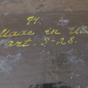 Op de afbeelding: Een close-up van een donkerbruin oppervlak met gele handgeschreven tekst. De tekst luidt "74: Made in USSR art. S-28."