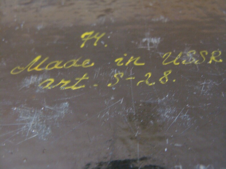 Op de afbeelding: Een close-up van een donkerbruin oppervlak met gele handgeschreven tekst. De tekst luidt "74: Made in USSR art. S-28."