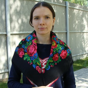 May include: A black shawl with a vibrant floral pattern featuring pink, red, blue, and yellow flowers. The shawl is worn around the neck and shoulders, creating a colorful contrast against the dark background.