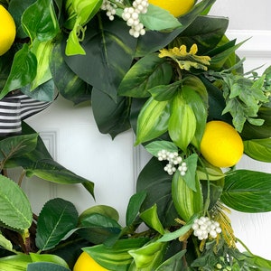 Puede incluir: Una corona de lim&oacute;n verde y amarillo con bayas blancas. La corona est&aacute; hecha de hojas y limones artificiales.