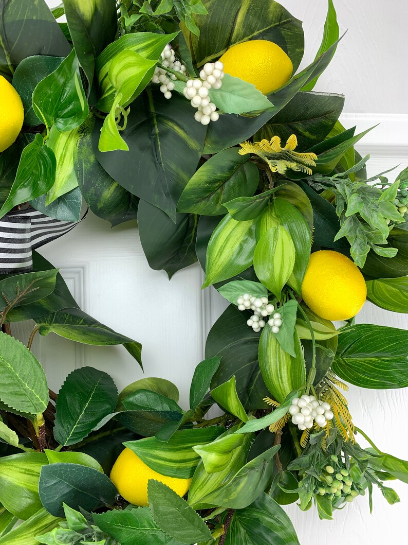 Puede incluir: Una corona de lim&oacute;n verde y amarillo con bayas blancas. La corona est&aacute; hecha de hojas y limones artificiales.