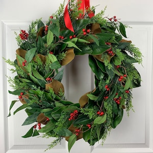 May include: A green Christmas wreath with magnolia leaves, cedar sprigs, and red berries.