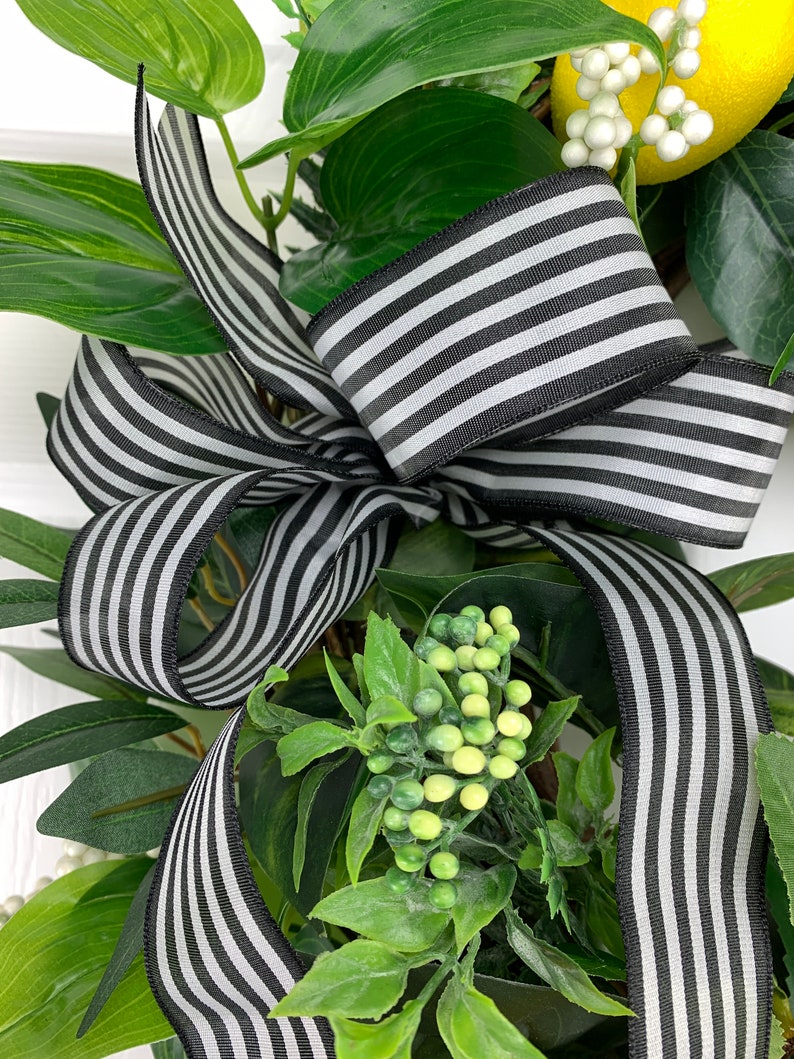 Puede incluir: Una cinta rayada en blanco y negro atada en un lazo, con hojas verdes y bayas blancas alrededor.