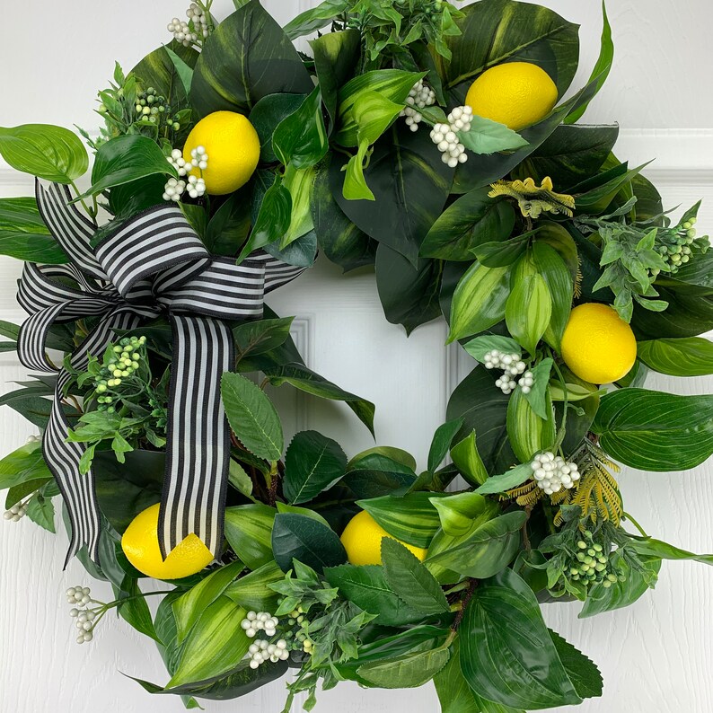 Puede incluir: Una corona de lim&oacute;n verde y amarilla con un lazo a rayas blanco y negro. La corona est&aacute; hecha de vegetaci&oacute;n artificial y limones.
