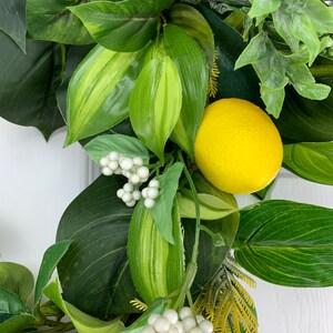 Puede incluir: Una corona artificial de lim&oacute;n verde y amarillo con bayas blancas. La corona est&aacute; hecha de hojas y frutos artificiales.
