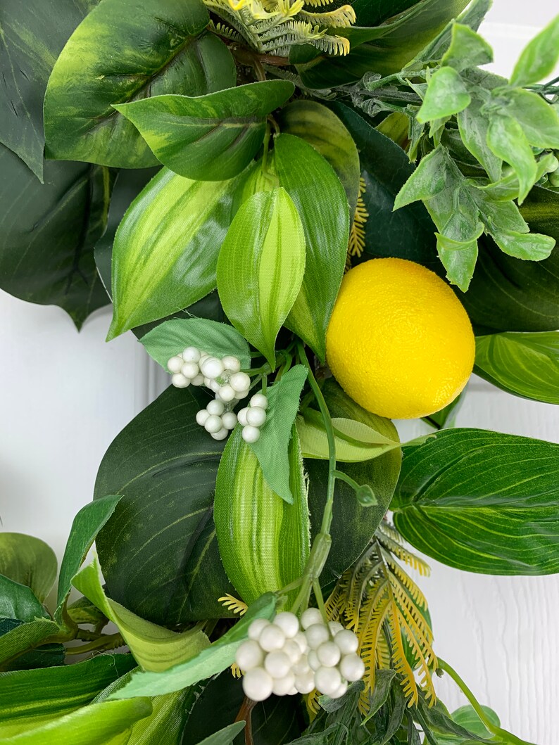 Puede incluir: Una corona artificial de lim&oacute;n verde y amarillo con bayas blancas. La corona est&aacute; hecha de hojas y frutos artificiales.