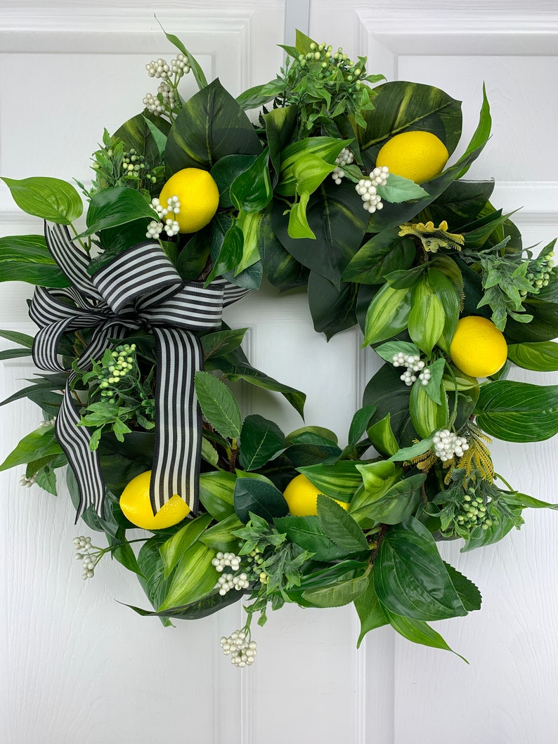 Puede incluir: Una corona de lim&oacute;n verde y amarilla con una cinta rayada en blanco y negro. La corona est&aacute; decorada con peque&ntilde;as flores blancas y hojas verdes.