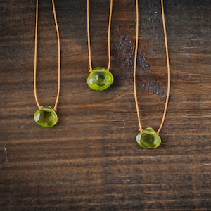 May include: Three necklaces with green gemstone pendants on a brown wooden background.