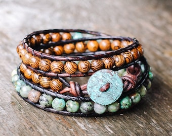 May include: A layered bracelet with brown wooden beads, turquoise stones, and a turquoise button. The bracelet is on a wooden surface.