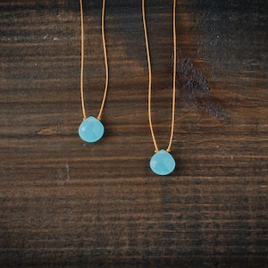 May include: Two delicate necklaces with light blue gemstone pendants on a dark brown wooden background.