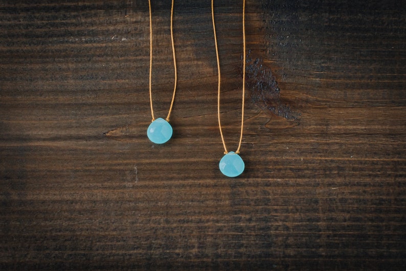 May include: Two delicate necklaces with light blue gemstone pendants on a dark brown wooden background.