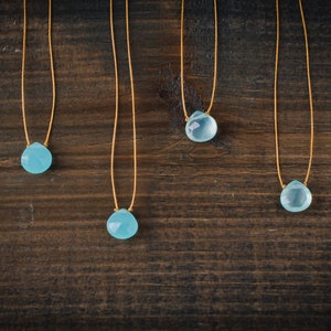May include: Four necklaces with light blue teardrop-shaped stones on a brown wooden background.