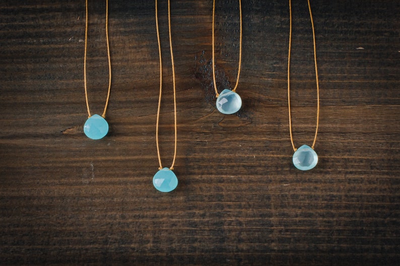 May include: Four necklaces with light blue teardrop-shaped stones on a brown wooden background.