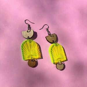 Peut inclure: Une paire de boucles d'oreilles géométriques en jaune néon et marron. Les boucles d'oreilles sont en acrylique et en bois. Les boucles d'oreilles sont en forme d'arches et de cercles.