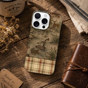 May include: A smartphone case featuring a printed design of a deer and ducks in a pond on the upper portion and a brown, tan, and green plaid pattern on the lower portion. The case has a white camera module cutout with three circular lenses.