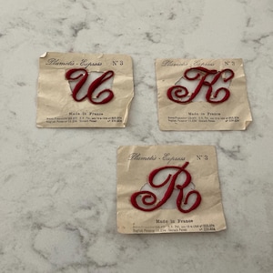 May include: Three individual red embroidered script letters U, K, and R, each mounted on a square beige paper backing labeled Plumetis-Express N° 3 Made in France with patent information printed in black text below the letter.